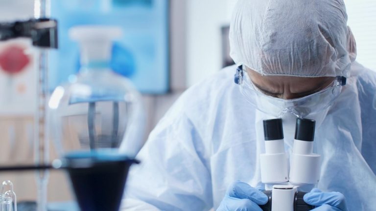 chemist researcher doctor wearing ppe equipment analyzing virus sample using microscope